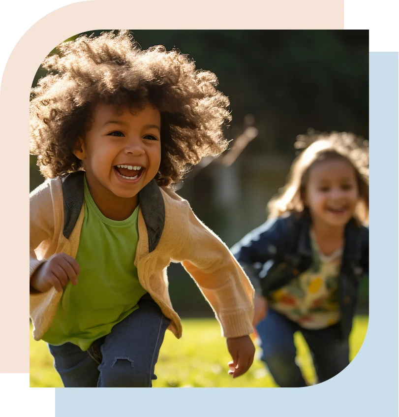 wo young children running happily on a grassy field toward the camera on a sunny day